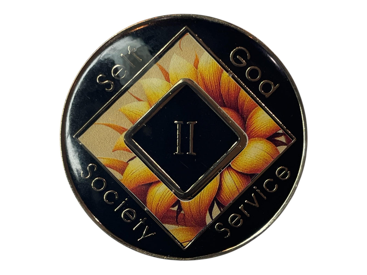 Narcotics Anonymous 2-year recovery medallion featuring a radiant sunflower background symbolizing warmth, renewal, and continued growth in sobriety. The design includes the NA logo at the center with a Roman numeral II representing two years clean, surrounded by the words “Self, God, Society, Service” on a sleek black enamel border that highlights balance and gratitude in recovery.
