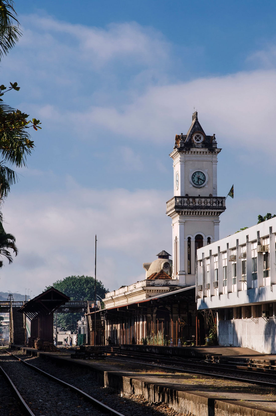 Historic railway station in Juiz de Fora, Minas Gerais, Brazil, featuring a clock tower, traditional station architecture, and railroad tracks beneath a bright sky.