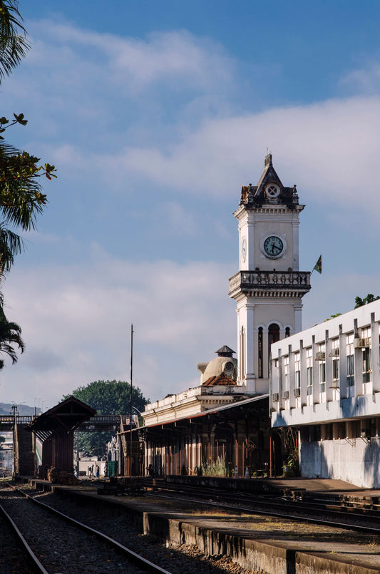Historic railway station in Juiz de Fora, Minas Gerais, Brazil, featuring a clock tower, traditional station architecture, and railroad tracks beneath a bright sky.
