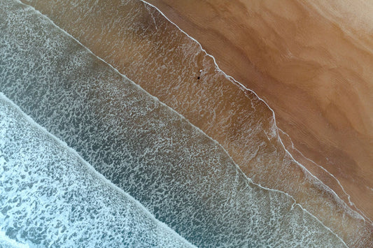 Aerial view of ocean waves rolling onto a sandy Gulf Coast beach in Galveston, Texas, with white surf meeting the shoreline.