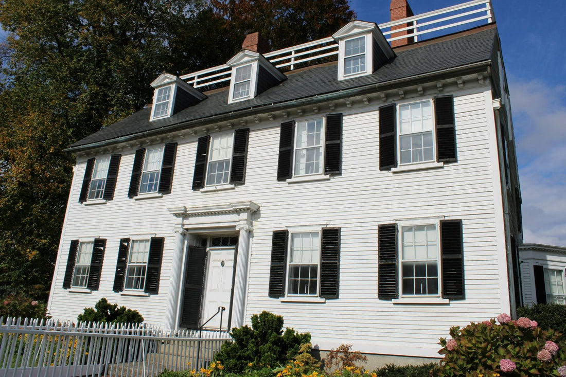 Historic white colonial house with black shutters and a white picket fence in Salem, Massachusetts.