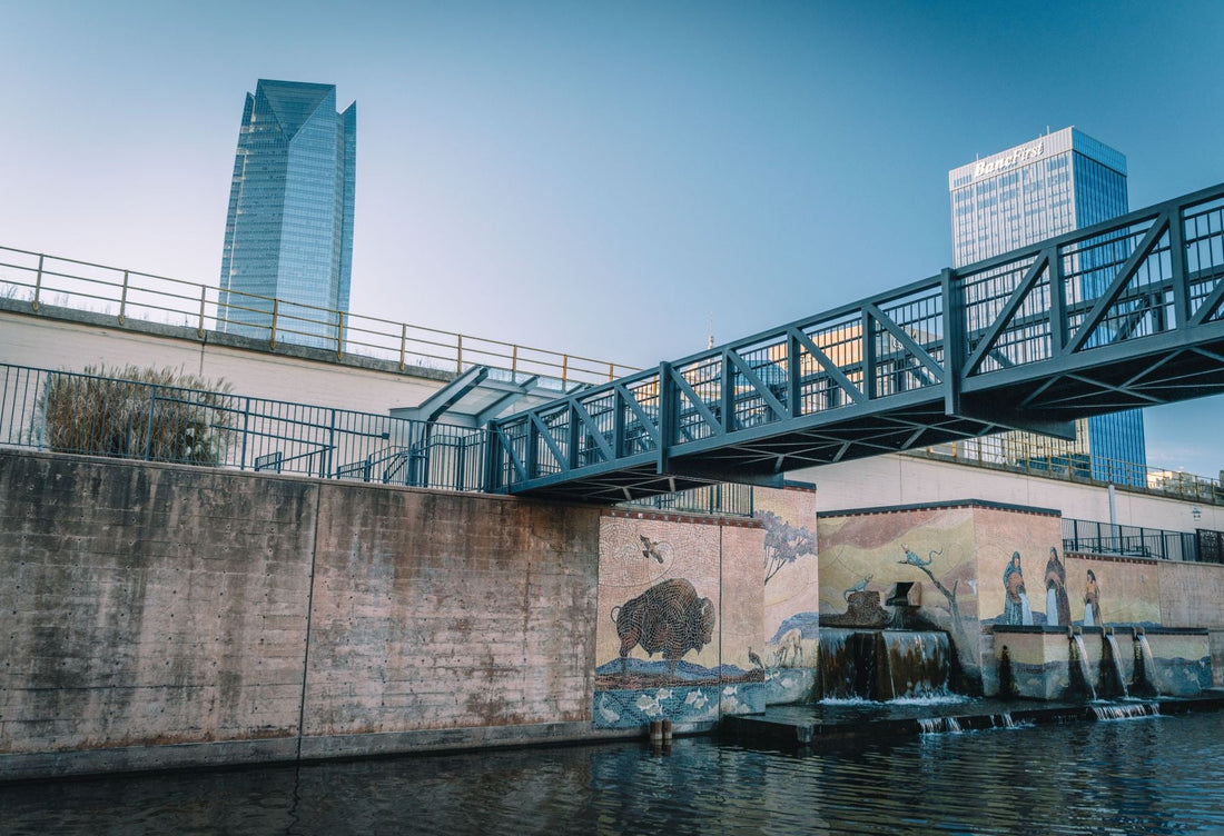 Oklahoma City canal with a pedestrian bridge, colorful murals and downtown skyscrapers in the background.
