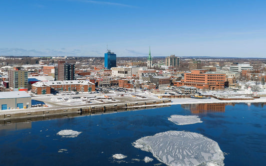 Downtown Trois-Rivières skyline along the riverfront with city buildings reflected in the water.
