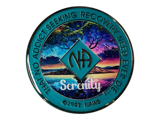 Narcotics Anonymous (NA) medallion featuring a colorful scenic design with a calm lake, tree silhouette, and vibrant sunset sky. The medallion has a teal border with the phrase 'That no addict seeking recovery need ever die' and the word 'Serenity' in white text, along with the NA logo in the center.