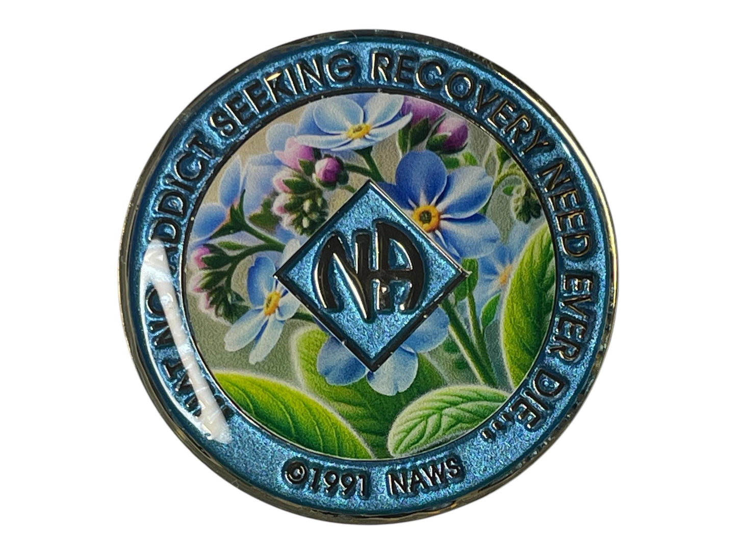 Narcotics Anonymous recovery medallion with blue border, NA diamond logo, and colorful floral background design featuring purple and yellow flowers with green leaves.