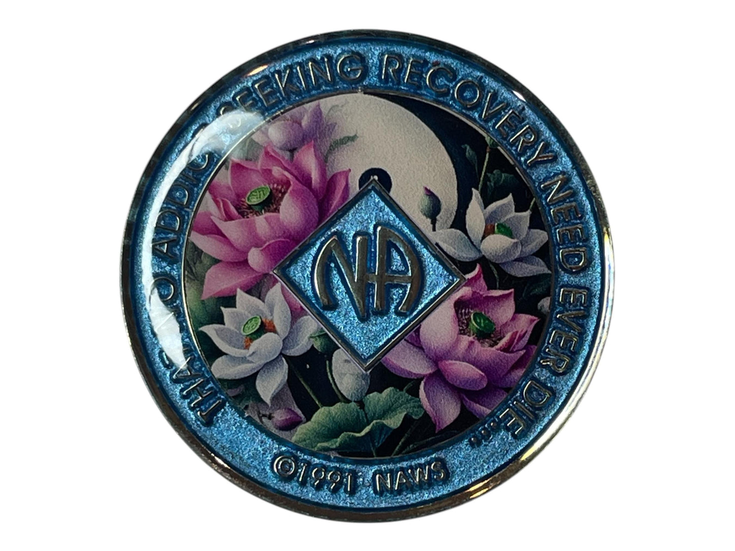 Narcotics Anonymous recovery medallion with shimmering blue border, NA diamond logo, and lotus flower design under a moon, featuring the phrase ‘That No Addict Seeking Recovery Need Ever Die