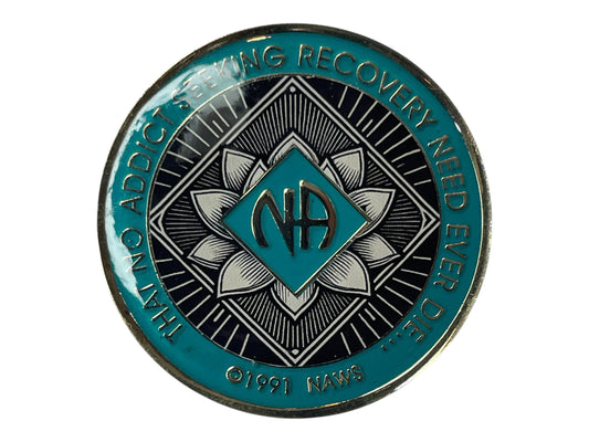 Narcotics Anonymous teal and black recovery medallion featuring a radiant lotus flower design with the NA logo in the center, symbolizing spiritual awakening, purity, and transformation in sobriety. Inscribed with “That No Addict Seeking Recovery Need Ever Die” and ©1991 NAWS.