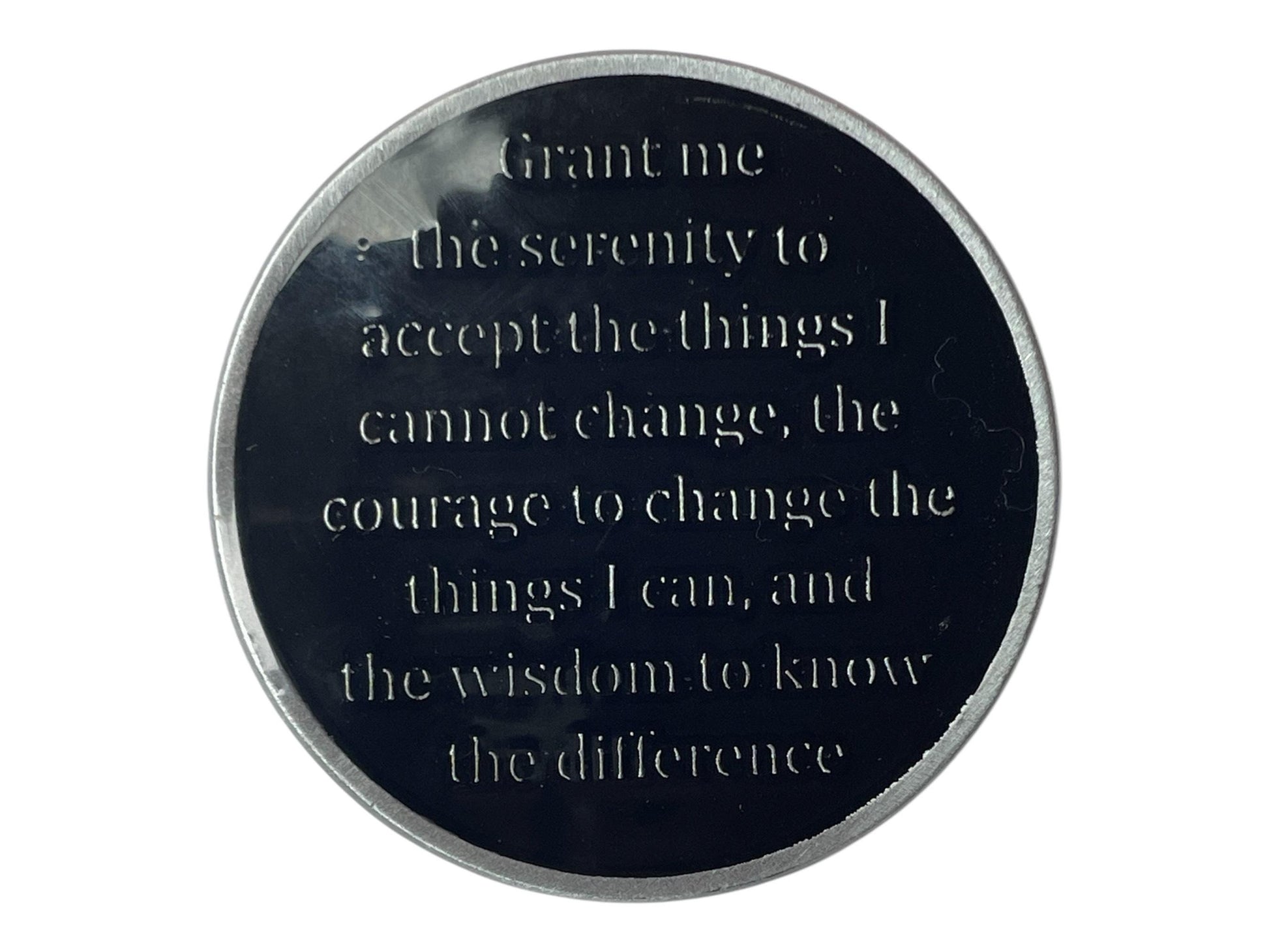 A black metal circular token with a silver rim. The token has the following text engraved on it: 'Grant me the serenity to accept the things I cannot change, the courage to change the things I can, and the wisdom to know the difference.'