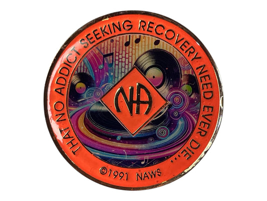 Narcotics Anonymous recovery medallion with vibrant orange border, NA diamond logo, and colorful music-themed artwork featuring vinyl records and musical notes, with the phrase ‘That No Addict Seeking Recovery Need Ever Die.’