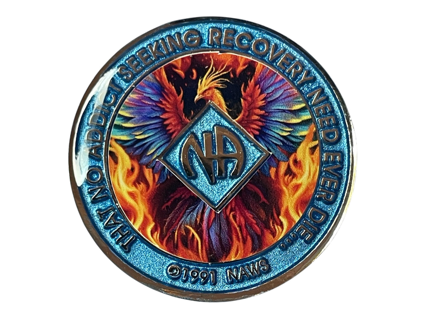 Narcotics Anonymous recovery medallion with shimmering blue border, NA diamond logo, and fiery phoenix artwork rising from flames, featuring the phrase ‘That No Addict Seeking Recovery Need Ever Die.’