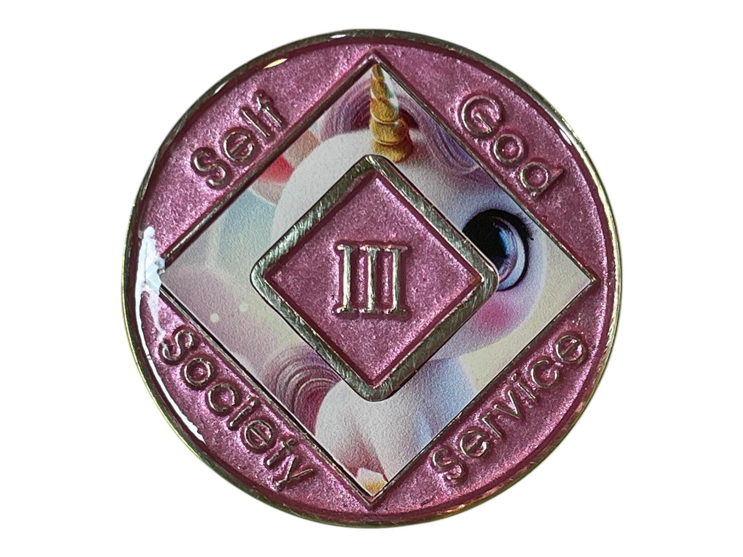 A pink metal coin with a unicorn image and a diamond shape in the center. The diamond shape has the Roman numeral 'III' in the center. The coin has the words 'self', 'society', 'service', and 'god' around the outside.