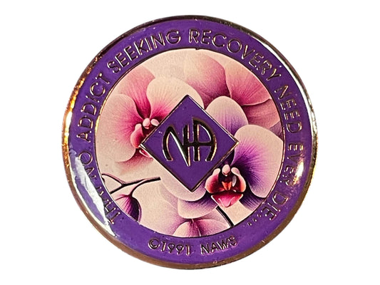 Narcotics Anonymous recovery medallion featuring elegant purple and pink orchid flowers symbolizing beauty, healing, and growth. The coin has a rich purple border engraved with “That No Addict Seeking Recovery Need Ever Die” and the NA logo in the center, representing serenity and renewal in recovery.