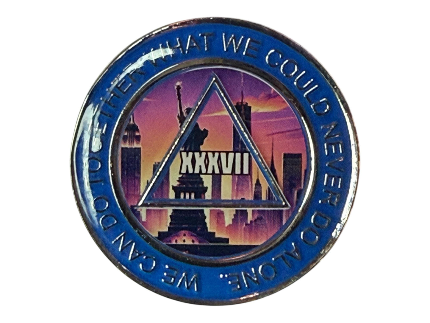 A blue and silver medallion with a cityscape design. The center features a triangle with the Roman numeral XXXVII. The words 'WE CAN DO TOGETHER WHAT WE COULD NEVER DO ALONE' are in a circular pattern around the edge. The background shows the Statue of Liberty and New York City skyline.