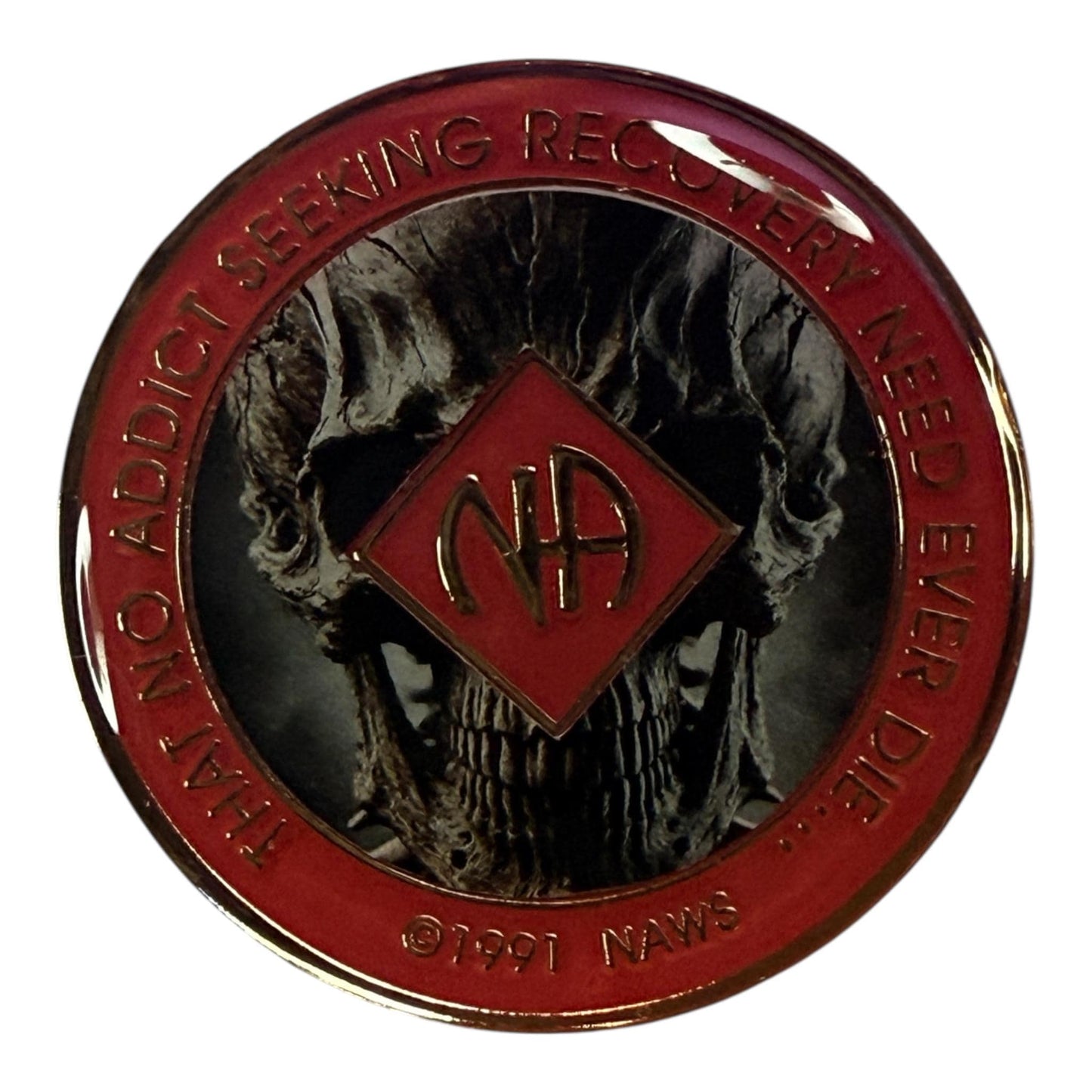 Narcotics Anonymous recovery medallion featuring a detailed skull design with a red enamel border and metallic finish. The NA logo is centered with the phrase “That No Addict Seeking Recovery Need Ever Die,” representing transformation, courage, and strength through addiction recovery.