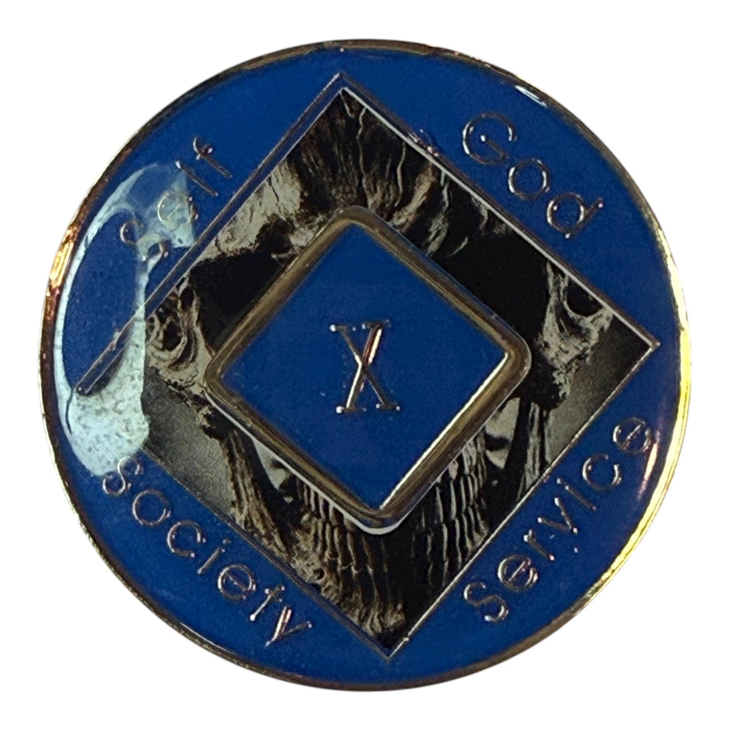 Narcotics Anonymous 10-year recovery medallion featuring a dark skull design with metallic detailing and a blue enamel border. The center diamond displays “X,” surrounded by the words “Self, God, Society, Service,” symbolizing a decade of strength, transformation, and perseverance in recovery.