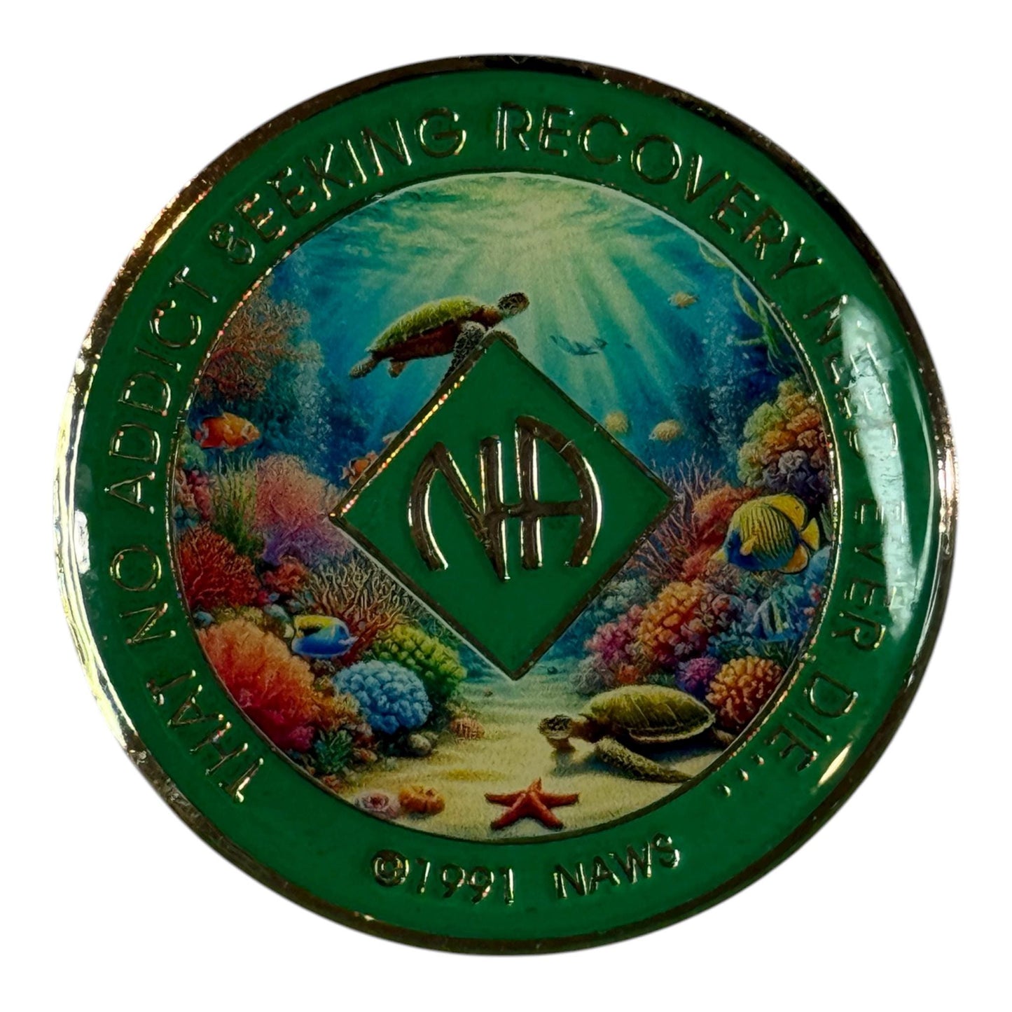 Narcotics Anonymous recovery medallion featuring an underwater sea turtle design surrounded by vibrant coral and ocean life. The coin has a shimmering green glitter border with the NA logo and the phrase “That No Addict Seeking Recovery Need Ever Die,” symbolizing peace, perseverance, and serenity in recovery.